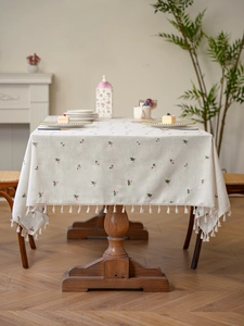 Detail of floral embroidery and cream tassel edge on linen tablecloth in home setting