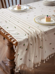 Close-up of cream linen tablecloth with pink floral embroidery and fringe edge