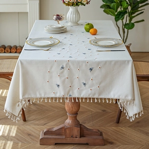 Cream embroidered linen tablecloth with tassels and bee patterns on a wooden table