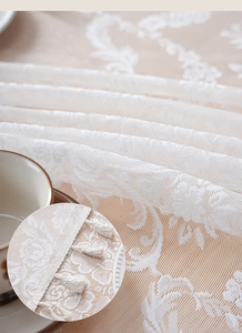 Detailed macro view of white floral lace tablecloth featuring delicate tassel edge trim