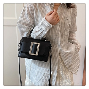 Detail of black pebbled leather crossbody bag featuring a large decorative metal buckle