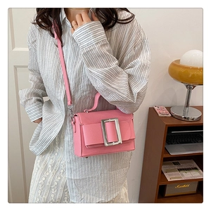 Detail of pink lychee grain leather handbag with large silver buckle on indoor background