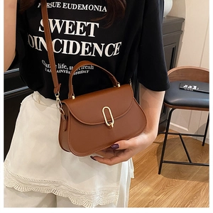 Detailed view of brown leather crossbody bag with gold U-shaped buckle on a model