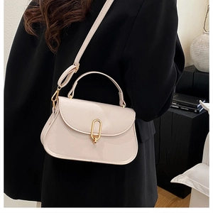 Detail of a cream structured crossbody bag with a gold metal clasp on a black blazer