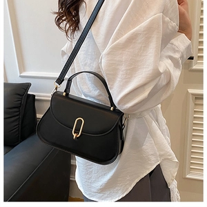Détail du sac à main en cuir noir avec fermoir doré ovale porté par un mannequin chic