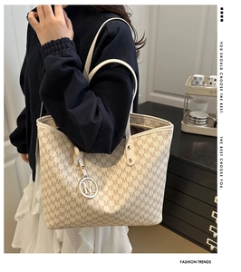 Detail of minimalist tote bag with monogram print and metallic M charm on the shoulder