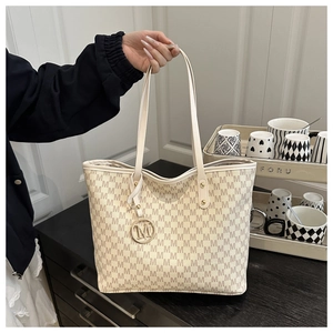 Detail of a beige tote bag with M-letter pattern and a circular metal logo charm