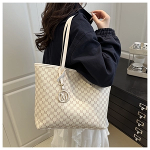 Close-up of beige tote bag with M-letter monogram print and golden metal charm detail
