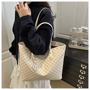 Detail of cream monogram tote bag with gold M-shaped metal charm and leather trim