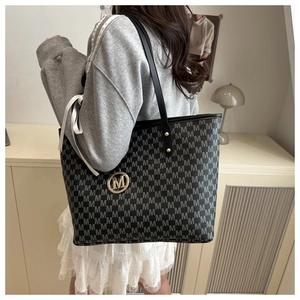 Close-up of stylish M-pattern tote bag with metallic logo charm and slim handles