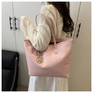 Detail of pink monogram tote bag with gold M-logo pendant shown on a model shoulder