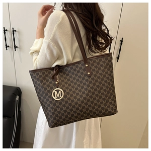 Detail of a brown tote bag featuring all-over M monogram and a gold letter pendant