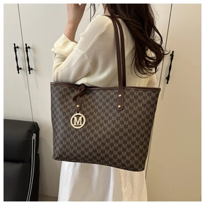 Shoulder shot of a brown monogram tote bag with gold M charm and leather straps