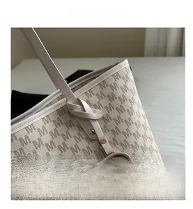 Detailed view of beige tote bag with monogram print and golden metal M charm logo