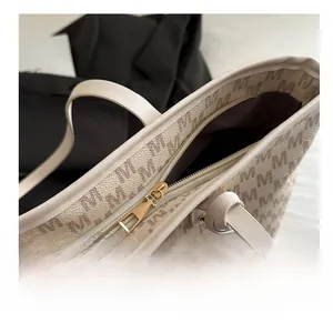 Close-up of smooth gold zipper and brown M letter print on beige leather tote bag