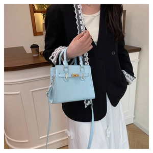 Detail of light blue patent leather bag with gold hardware held by model in cafe
