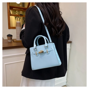 Detail of light blue crossbody bag with golden twist lock on a black blazer background