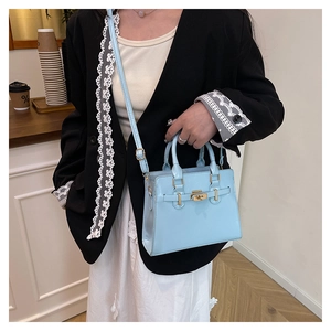 Detail of light blue glossy handbag with golden turn-lock and elegant twin handles