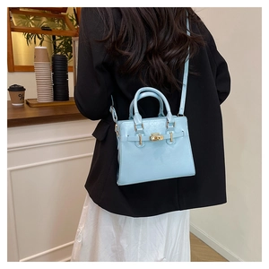 Model wearing a light blue glossy leather handbag over a black blazer in a cafe