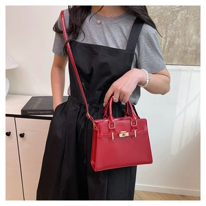Close-up of a red glossy leather handbag featuring golden clasp and detachable shoulder strap