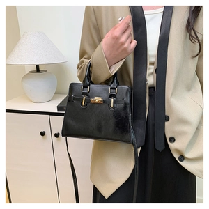 Detail of glossy black handbag with gold metal clasp and elegant top handle strap