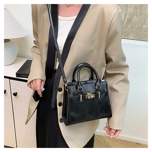 Detailed view of black leather handbag with gold lock and sleek shoulder strap styling