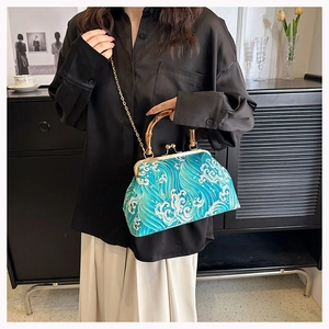 Detailed view of wave pattern bag with bamboo handle and gold chain on person
