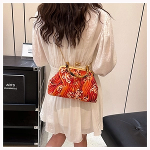 Detail of red sea-wave silk bag with bamboo handle and gold chain on model's shoulder