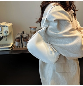 Sac sous le bras chic en cuir verni blanc brillant tenu par un mannequin dans un café