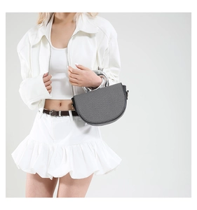 Graue Satteltasche mit Seidenband am Griff präsentiert auf einem weißen minimalistischen Outfit