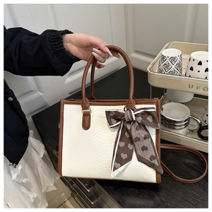 Close-up of beige faux snake leather handbag with brown trim and patterned silk scarf