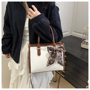 Detail of white crocodile pattern tote bag with brown trim and silk scarf on handle