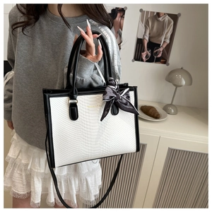 Close-up of black and white snakeskin tote bag with elegant bow tie and gold text