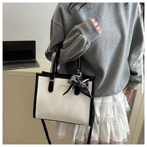 Detail showing snake skin texture and a black white ribbon on a chic square handbag