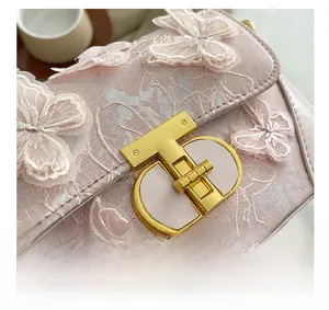Detail of golden T-lock and 3D butterfly embroidery on a pink crossbody bag