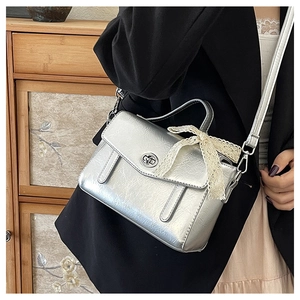 Dettaglio borsa a tracolla argento metallizzato con fiocco in pizzo bianco e logo in metallo