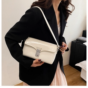 Fashionable white leather crossbody bag with silver buckle worn by a model in a suit
