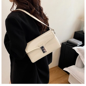 Detail of a creamy white shoulder bag with a silver metallic clasp worn with a black blazer
