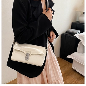 Detailed view of beige glossy leather shoulder bag with silver clasp worn by a model