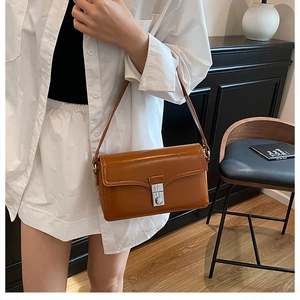 Close-up of brown leather baguette bag with silver metal buckle on a model shoulder