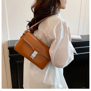 Detailed side view of brown leather crossbody bag with silver lock on white wall background