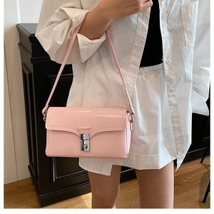 Detail of pink glossy shoulder bag featuring silver metal buckle on a white shirt model