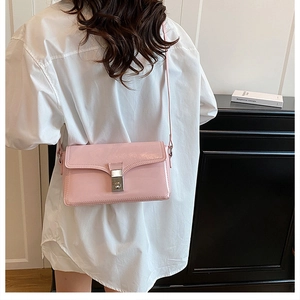 Pink glossy PU leather crossbody bag with silver buckle shown on shoulder of a model