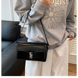 Side view of a classic black glossy shoulder bag with silver buckle worn by a model
