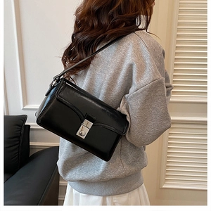 Glossy black underarm bag with silver square clasp shown in a modern interior setting