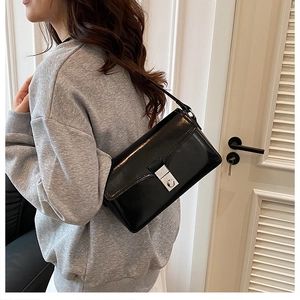 Detail view of the glossy black faux leather shoulder bag with a silver twist lock buckle