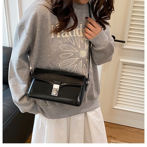 Close-up of a glossy black crossbody bag featuring a silver metal twist-lock and slim strap