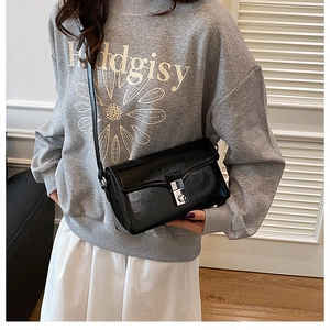Detail of glossy black leather crossbody bag with silver buckle and thin shoulder strap