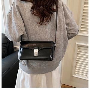 Detailed side view of a black patent leather shoulder bag with a silver metal clasp
