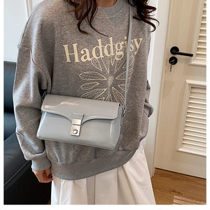 Detail of light blue crossbody bag with silver square metal lock and glossy finish